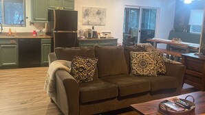 Un salon chaleureux avec un canapé, une table basse et un coin cuisine à l’arrière-plan.