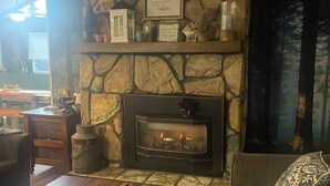 Un salon chaleureux avec une cheminée en pierre, un ventilateur de plafond et un canapé confortable.