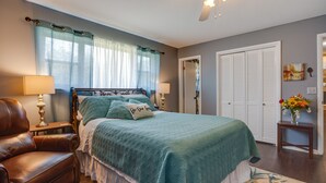 Ein Schlafzimmer mit einem Bett, einem Sessel, einem Nachttisch, einer Lampe, einem Deckenventilator und einer Tür.
