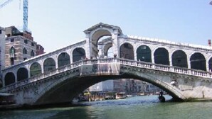A stone bridge with multiple arches over a body of water, surrounded by buildings.
