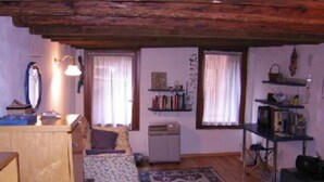 A cozy living room with a wooden ceiling, a sofa, a small table, a bookshelf, and a patterned rug.
