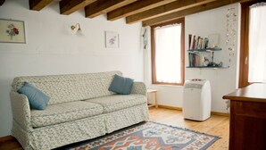 A living room with a floral-patterned sofa, a patterned rug, a bookshelf, and a radiator.