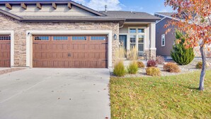 A two-story house with a stone facade, a large garage, and a well-maintained lawn with autumn foliage. - 8 Mi to USAFA! Townhome w/ Game Room & Backyard (Colorado Springs)