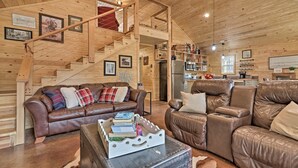 A spacious living area with a wooden staircase, leather sofas, and a rustic kitchen. - Peaceful Family Cabin on 10 Acres w/ Game Room! (Heflin)