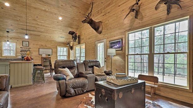 A rustic cabin interior with leather sofas, a wooden ceiling, and mounted animal heads. - Peaceful Family Cabin on 10 Acres w/ Game Room! (Heflin)