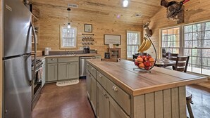 A kitchen with a wooden ceiling, a stainless steel refrigerator, a wooden island, and a wall-mounted turkey. - Peaceful Family Cabin on 10 Acres w/ Game Room! (Heflin)