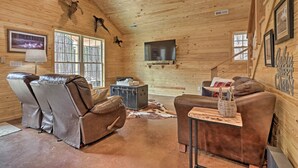 A cozy cabin interior with wooden walls, leather recliners, a flat-screen TV, and a rustic decor including mounted animal heads. - Peaceful Family Cabin on 10 Acres w/ Game Room! (Heflin)