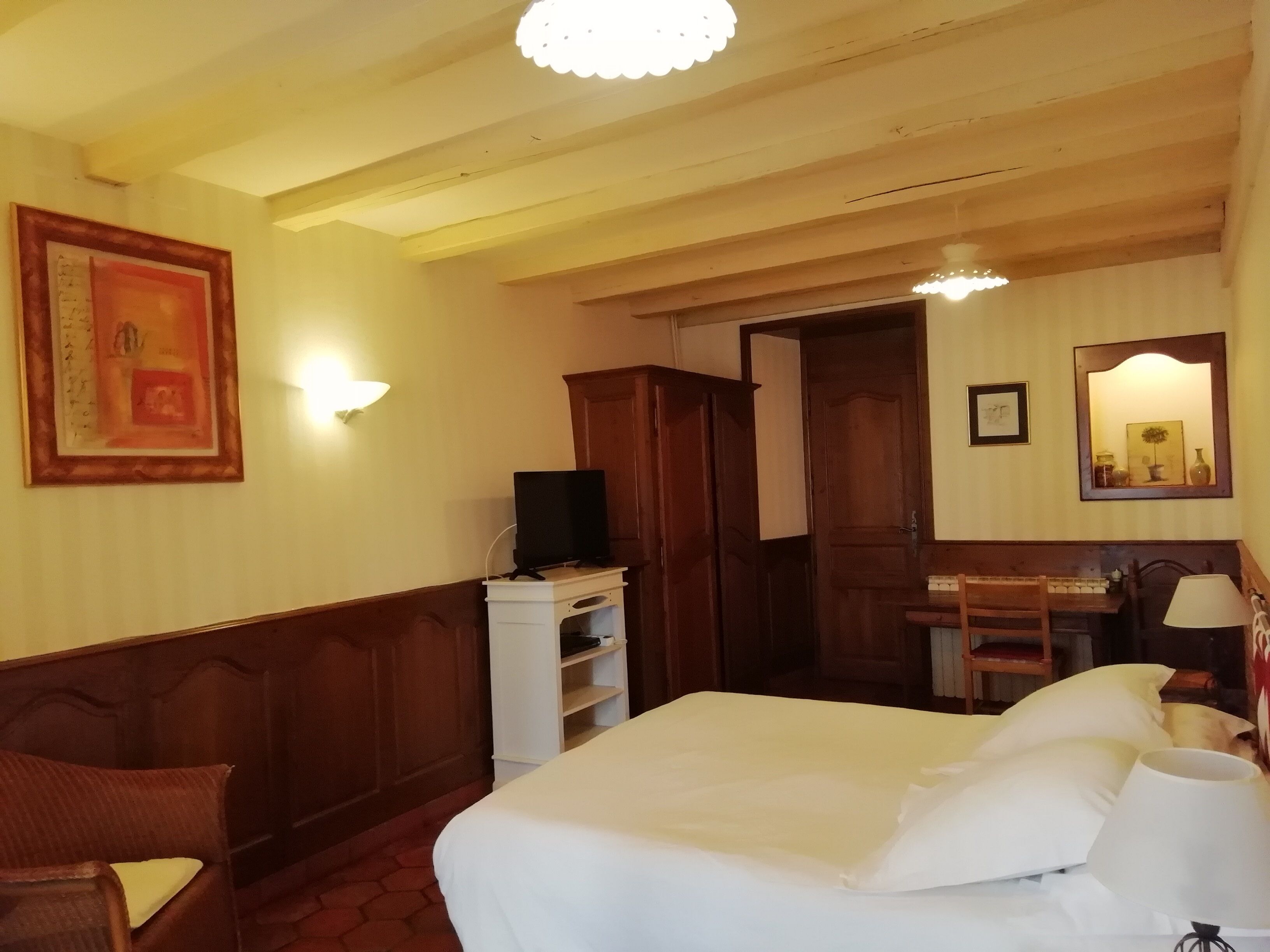 A hotel room with a bed, a desk, a chair, a television on a stand, and a mirror on the wall.