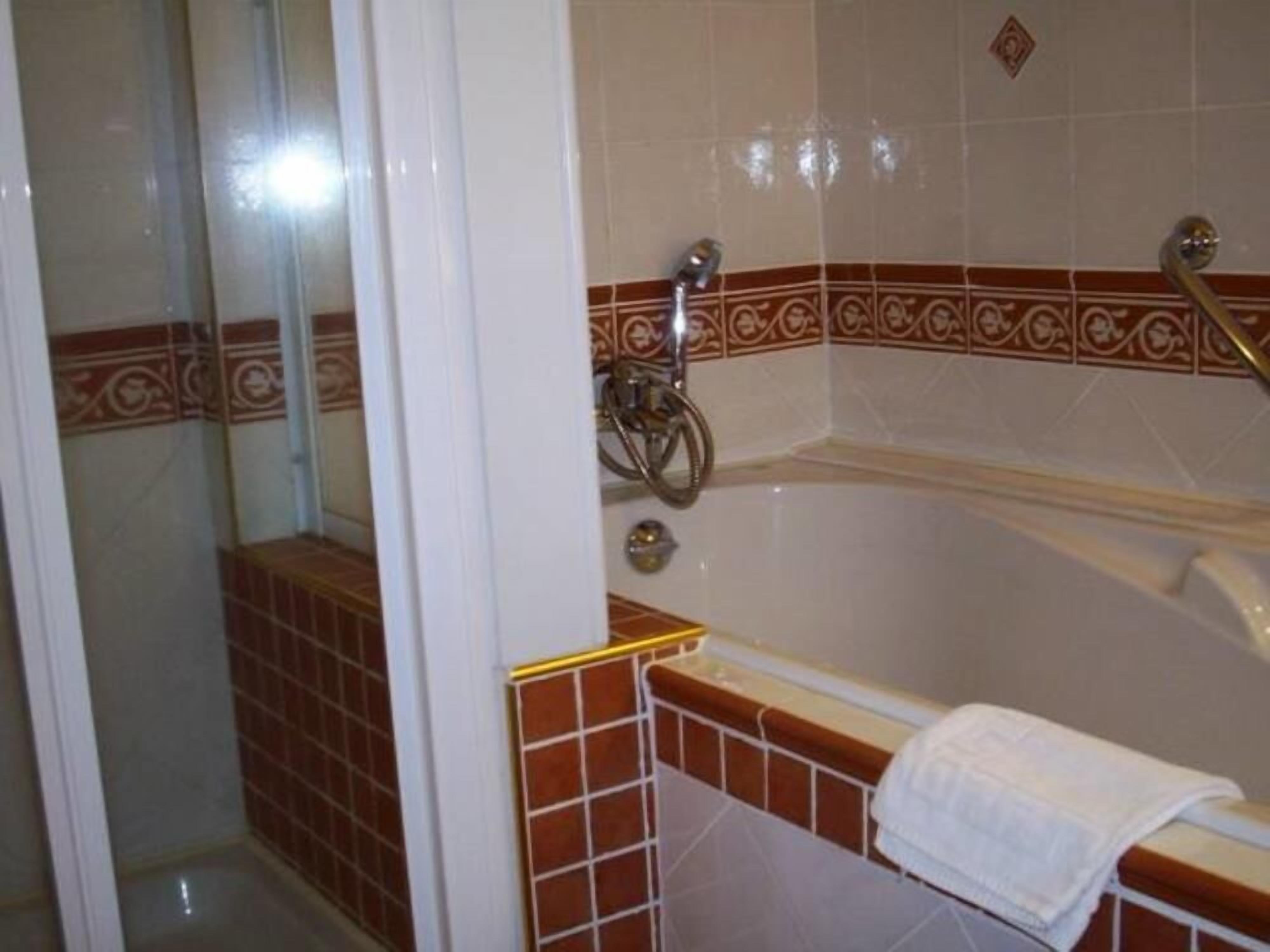 Un baño con bañera, zona de ducha y una toalla sobre el borde de la bañera.