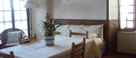 Une pièce comprenant un lit, une table, des chaises, une plante en pot, une lampe et un radiateur.