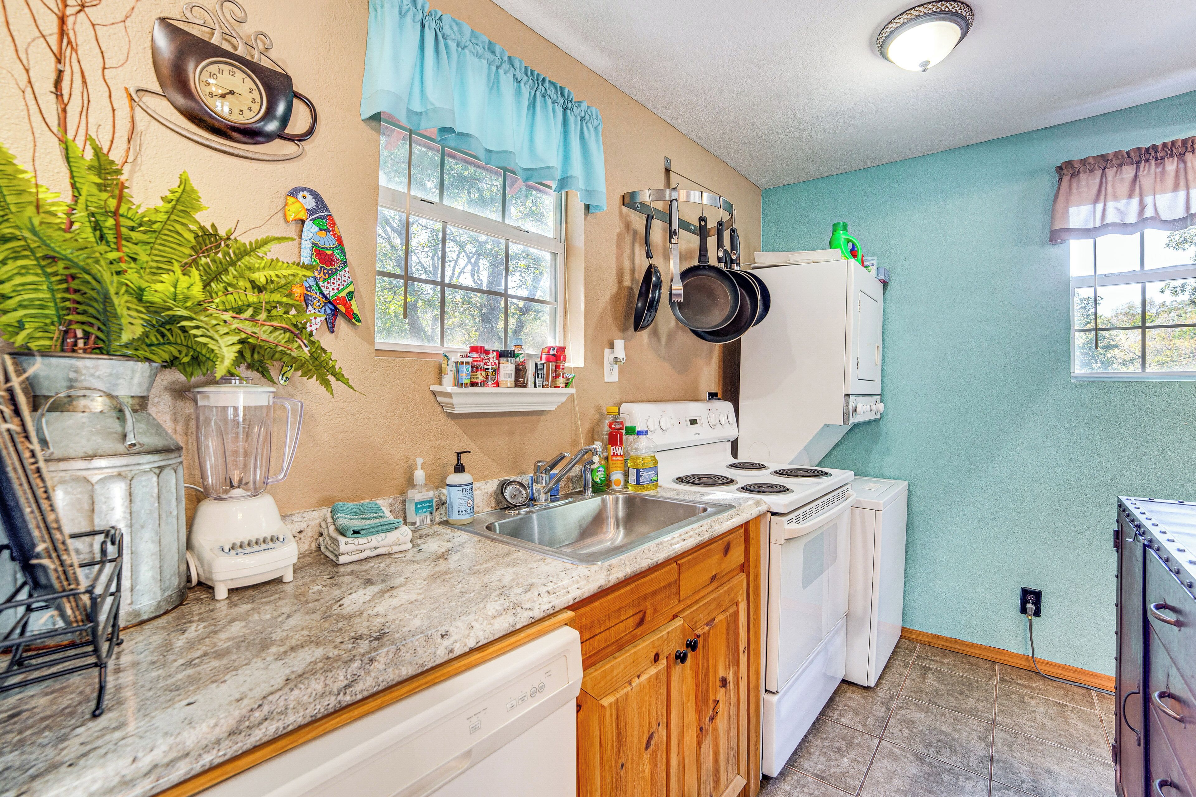 A kitchen with a granite countertop, white appliances, wooden cabinets, and a window with curtains.