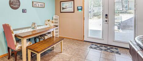A dining area with a wooden bench, a table, and chairs. There is a door with a glass panel and a view of the outside.