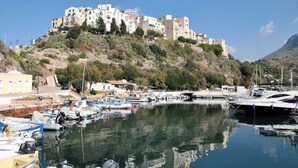 A coastal town with a prominent building on a hill, a marina with boats, and a clear sky.