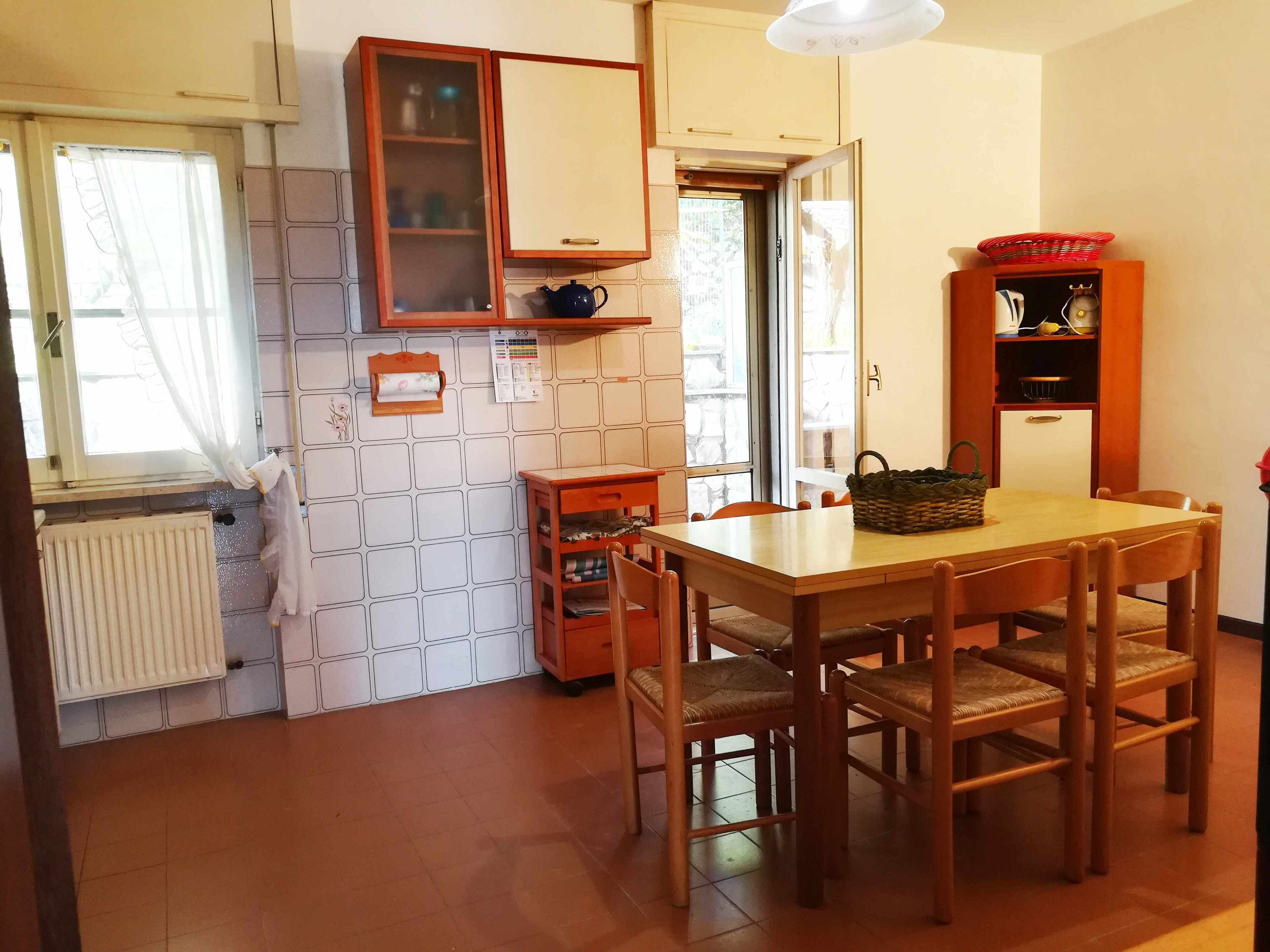 Une cuisine avec une table et des chaises en bois, un radiateur, une fenêtre avec des rideaux et un meuble avec des portes en verre.