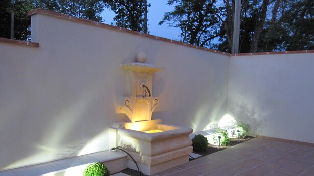 A fountain with a light, surrounded by a tiled patio and small plants.