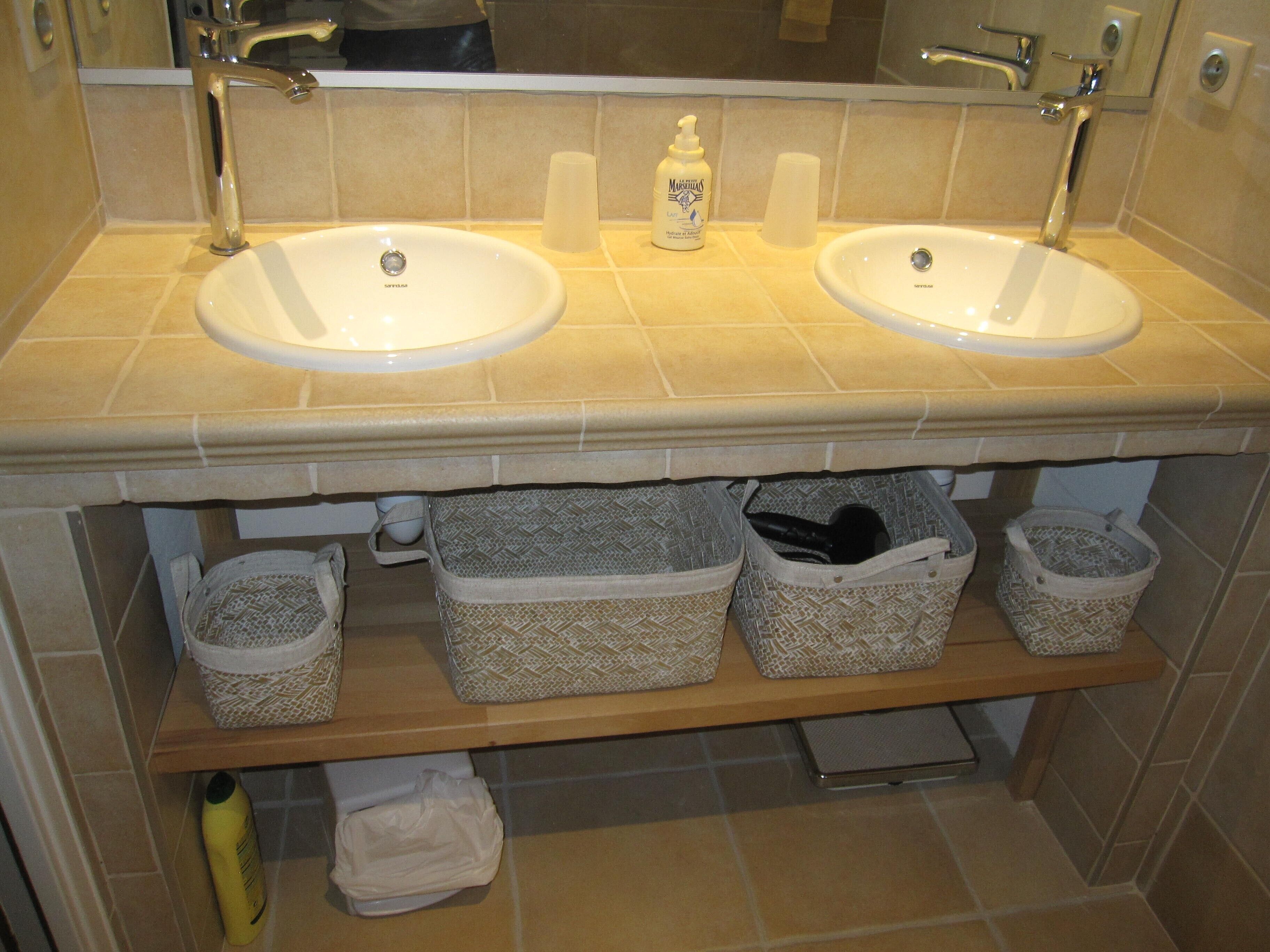 A bathroom with two sinks, a mirror, and storage baskets under the sink.