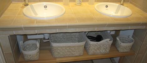 A bathroom with two sinks, a mirror, and storage baskets under the sink.