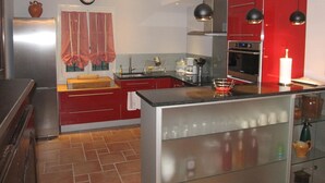 A modern kitchen with red cabinetry, stainless steel appliances, and a glass island.