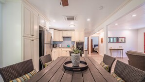 A modern kitchen with white cabinets, a stainless steel refrigerator, and a dining area with a wooden table and wicker chairs. - Suncrest House near beautiful Trinity Alps Wilderness Area (Junction City)