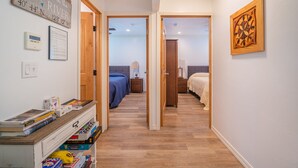 A hallway leading to a bedroom with a bed, bedside table, and a nightstand. There is a wooden door on the left, a wall clock, and a framed sign on the wall. - Suncrest House near beautiful Trinity Alps Wilderness Area (Junction City)