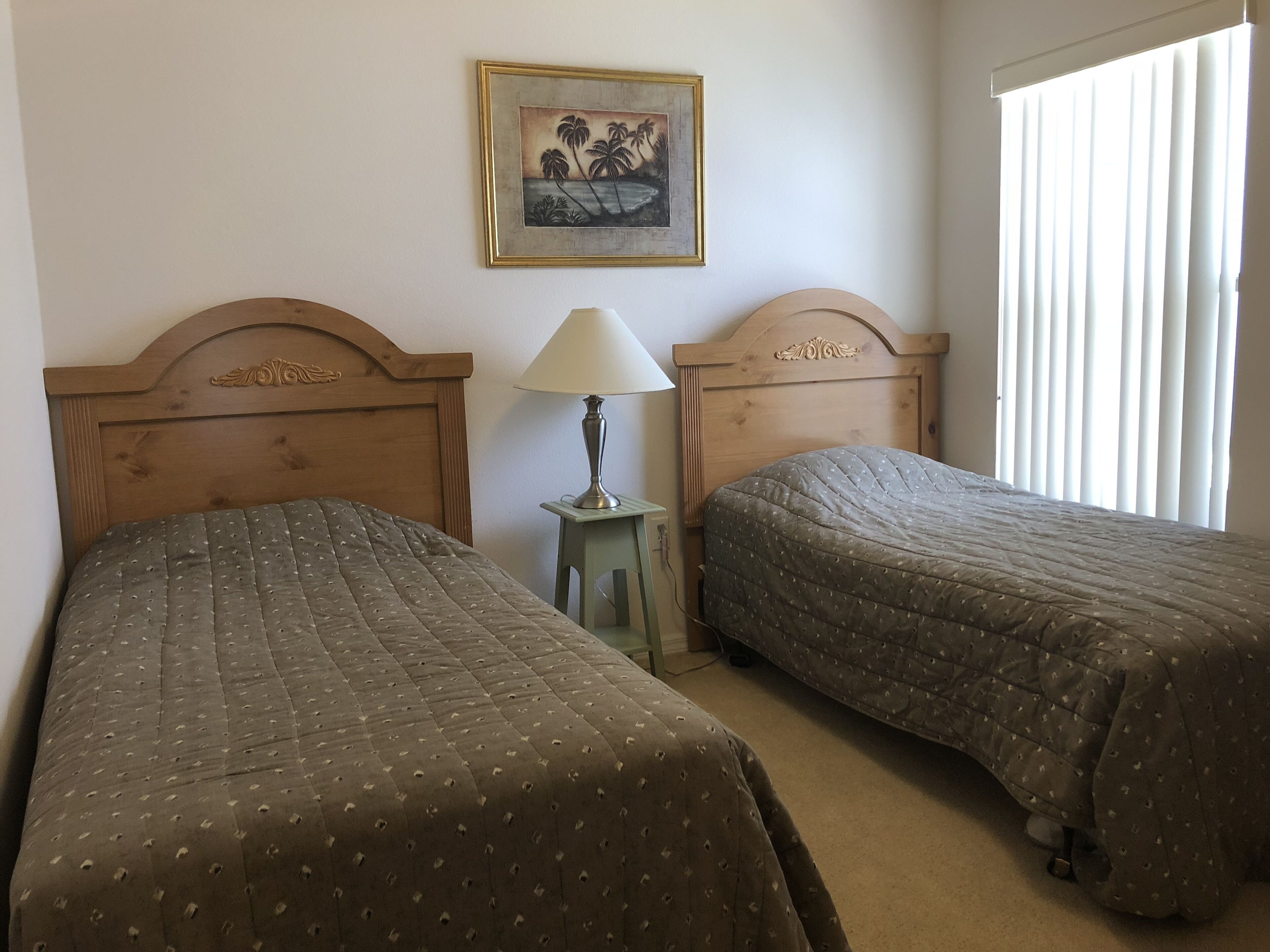 A room with two wooden beds, a small table with a lamp, and a framed picture on the wall.