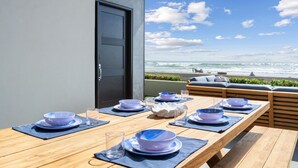 Una mesa de madera con cuencos y platos azules, un vaso y un adorno blanco, con vista a una playa y cielo despejado.