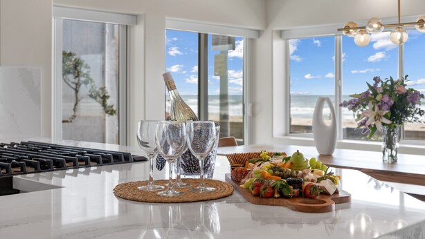 Una cocina con vista a la playa, una botella de champán y una bandeja de frutas en la encimera.