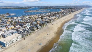 Vista aérea de un pueblo costero con una playa de arena extensa, un puerto deportivo con barcos y edificios residenciales a lo largo de la costa.