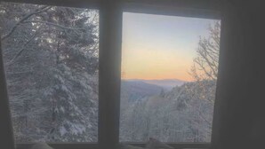 Una habitación con un amplio ventanal con vistas a un paisaje nevado al atardecer.