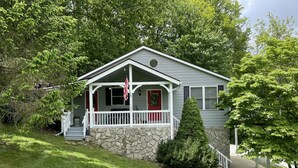 Une maison de plain-pied avec des fondations en pierre, une véranda dotée de balustrades blanches et une porte rouge.