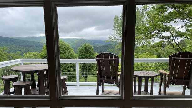 Une terrasse offrant une vue sur un paysage montagneux. On y trouve quatre chaises en bois et deux petites tables rondes.