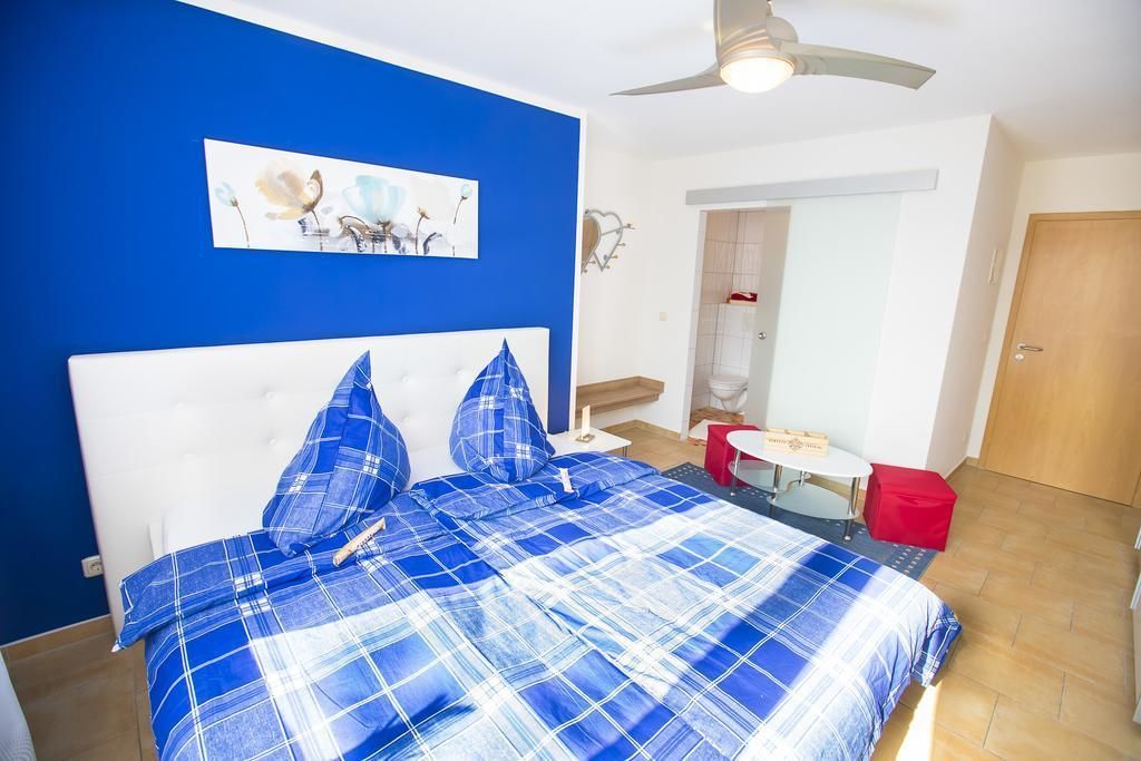 Een slaapkamer met een blauw-wit geruite sprei, een wit hoofdeinde en een plafondventilator.