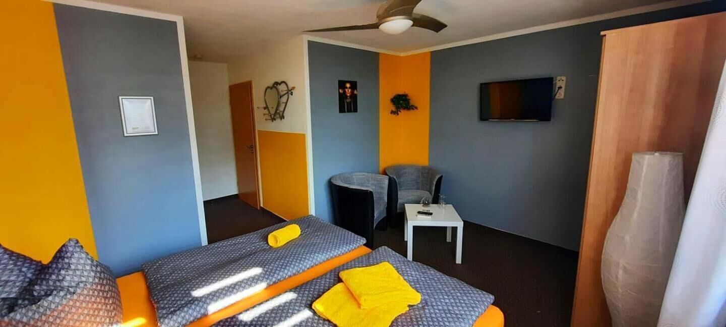 Habitación de hotel con dos camas, una mesita, una silla, televisión y ventilador de techo.