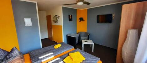 Habitación de hotel con dos camas, una mesita, una silla, televisión y ventilador de techo.