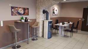 A modern cafe with a stone wall, bar stools, a coffee station, and a dining area with chairs and tables. - Pension Village (Naumburg)