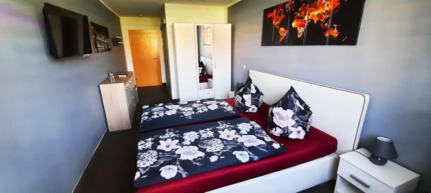 A bedroom with a bed, a nightstand, a TV, and a door leading to another room.