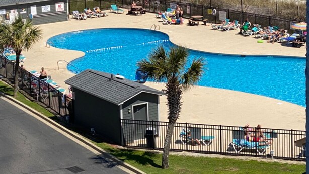 Zona de piscina con vista a la playa, piscina cercada y sillas de playa.