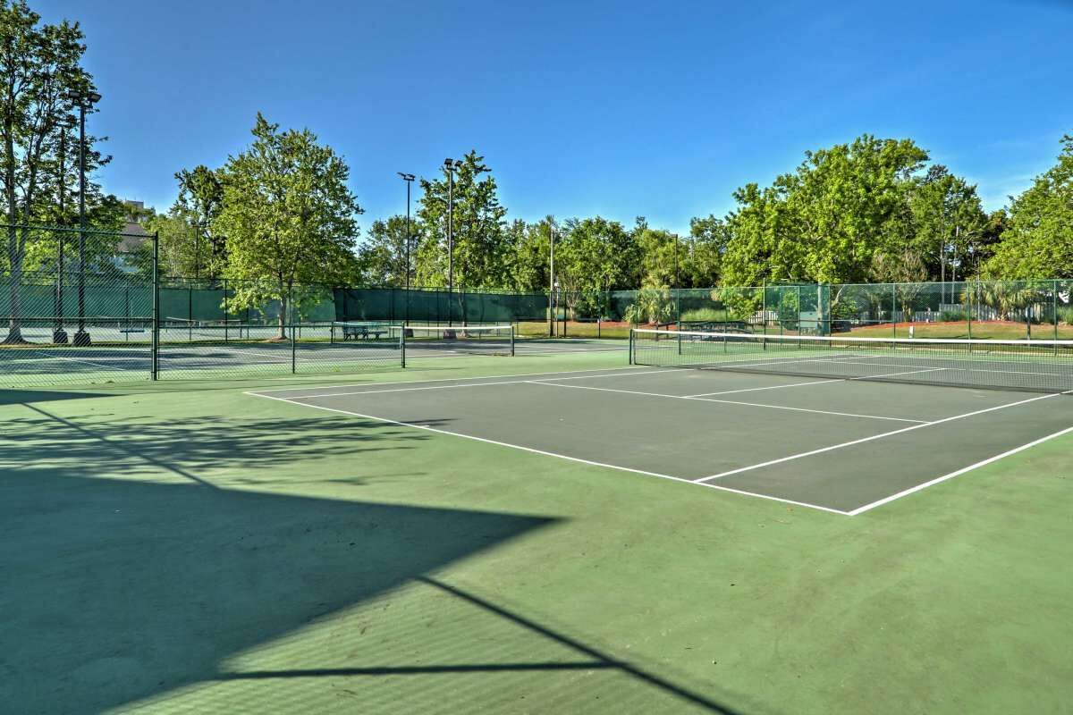 A tennis court with a net, surrounded by trees and a fence.
