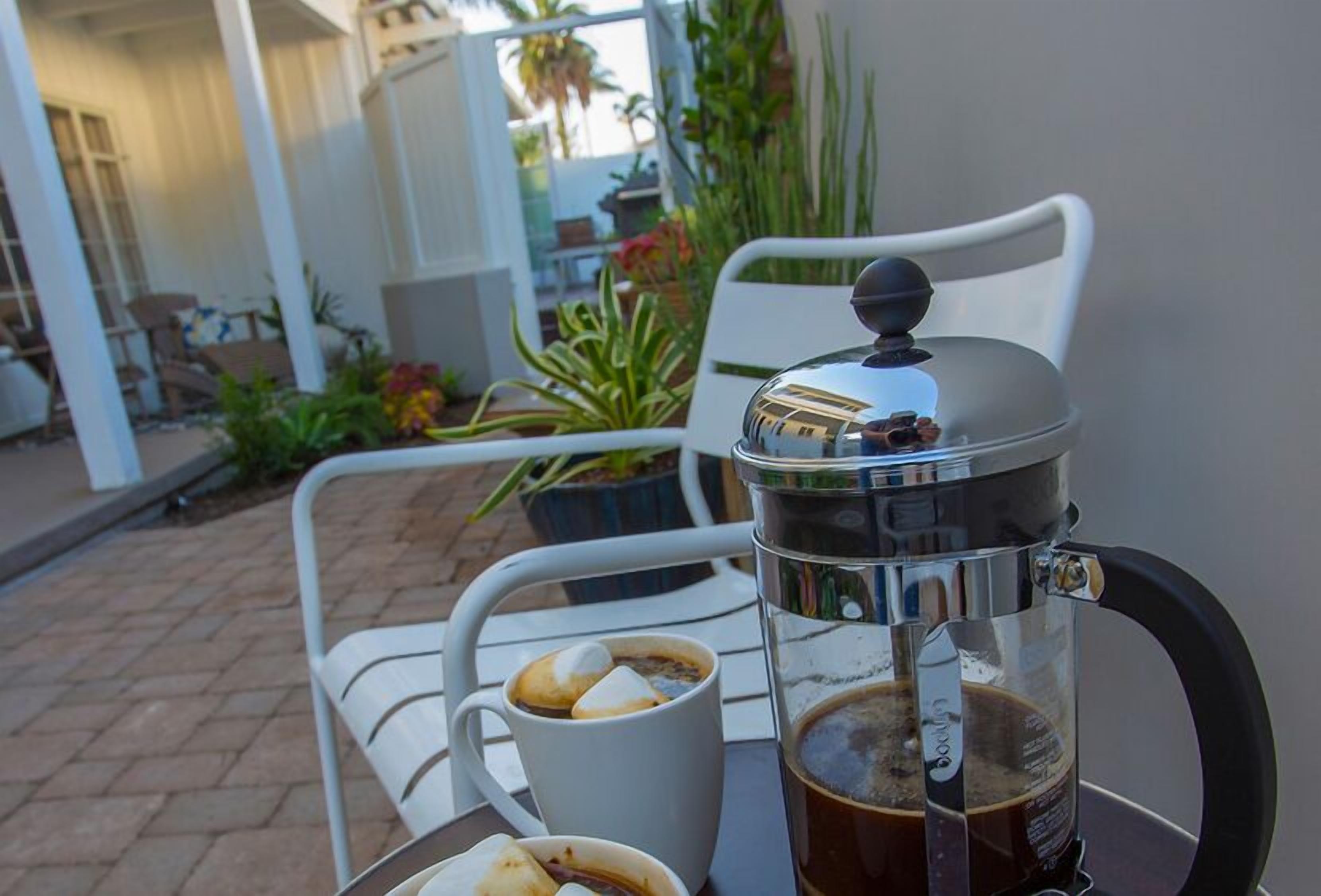 A coffee maker on a table with a cup of coffee and a plate of food.