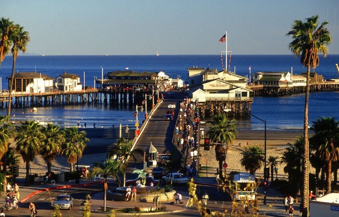 A pier extending into the water with buildings and palm trees along its length.