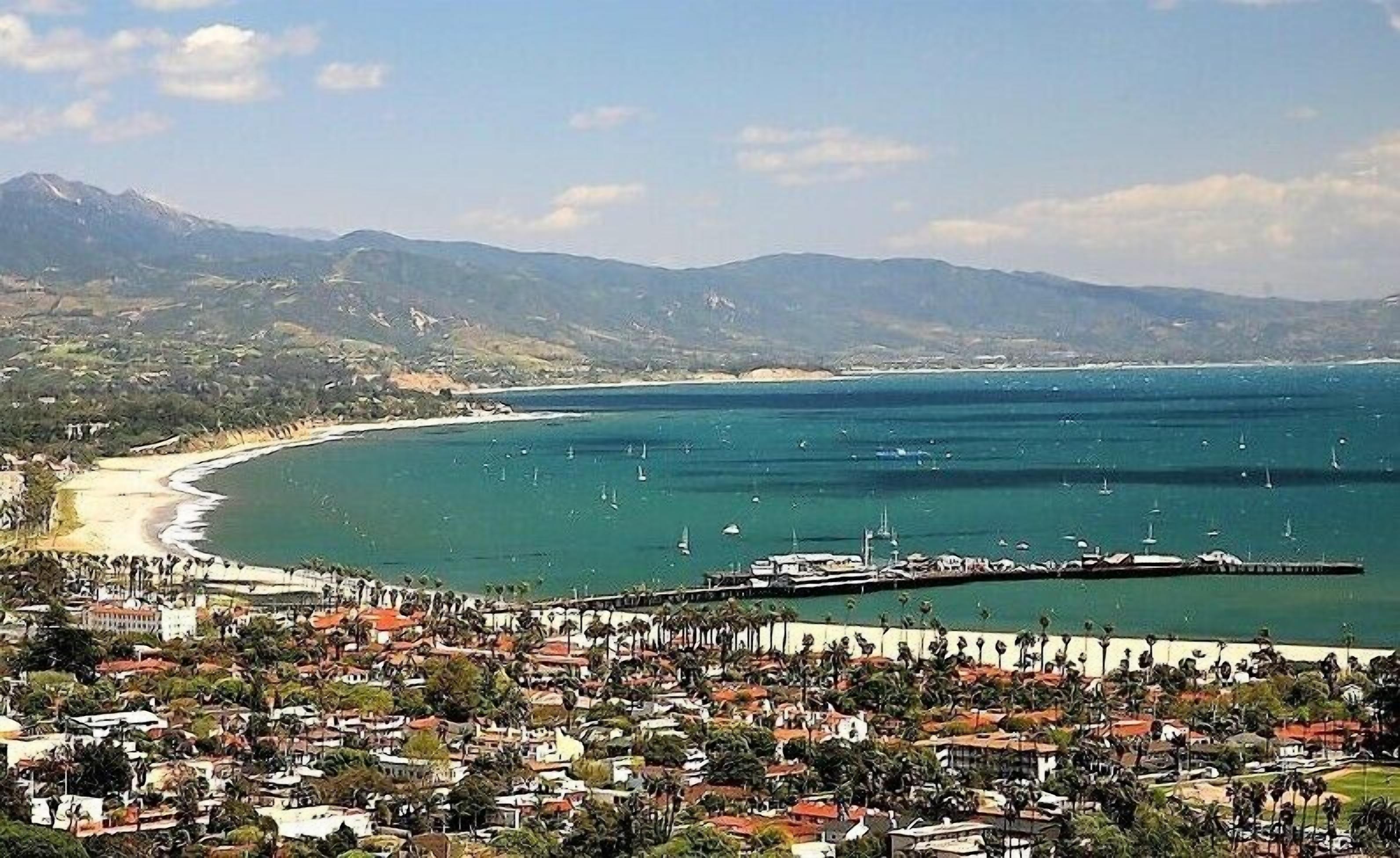 A coastal town with a pier extending into the sea, surrounded by residential buildings and a beach.