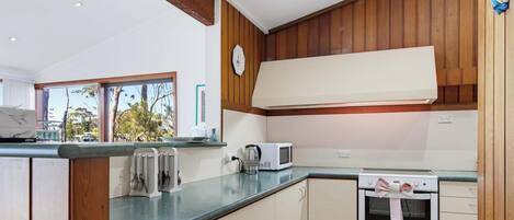 Une cuisine avec des meubles en bois, un four à micro-ondes, un four traditionnel et une fenêtre donnant sur les arbres.