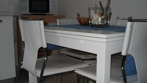 Een eettafel met stoelen, een glazen schaal met schelpen en een magnetron op de achtergrond.