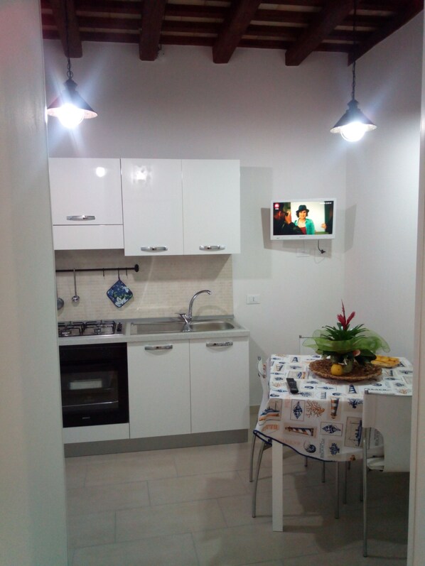 A compact kitchen with white cabinets, a sink, a stove, and a small table with a decorative plant.