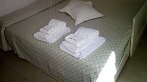 Een net opgemaakt bed met een geruit sprei, twee kussens en drie opgevouwen handdoeken.