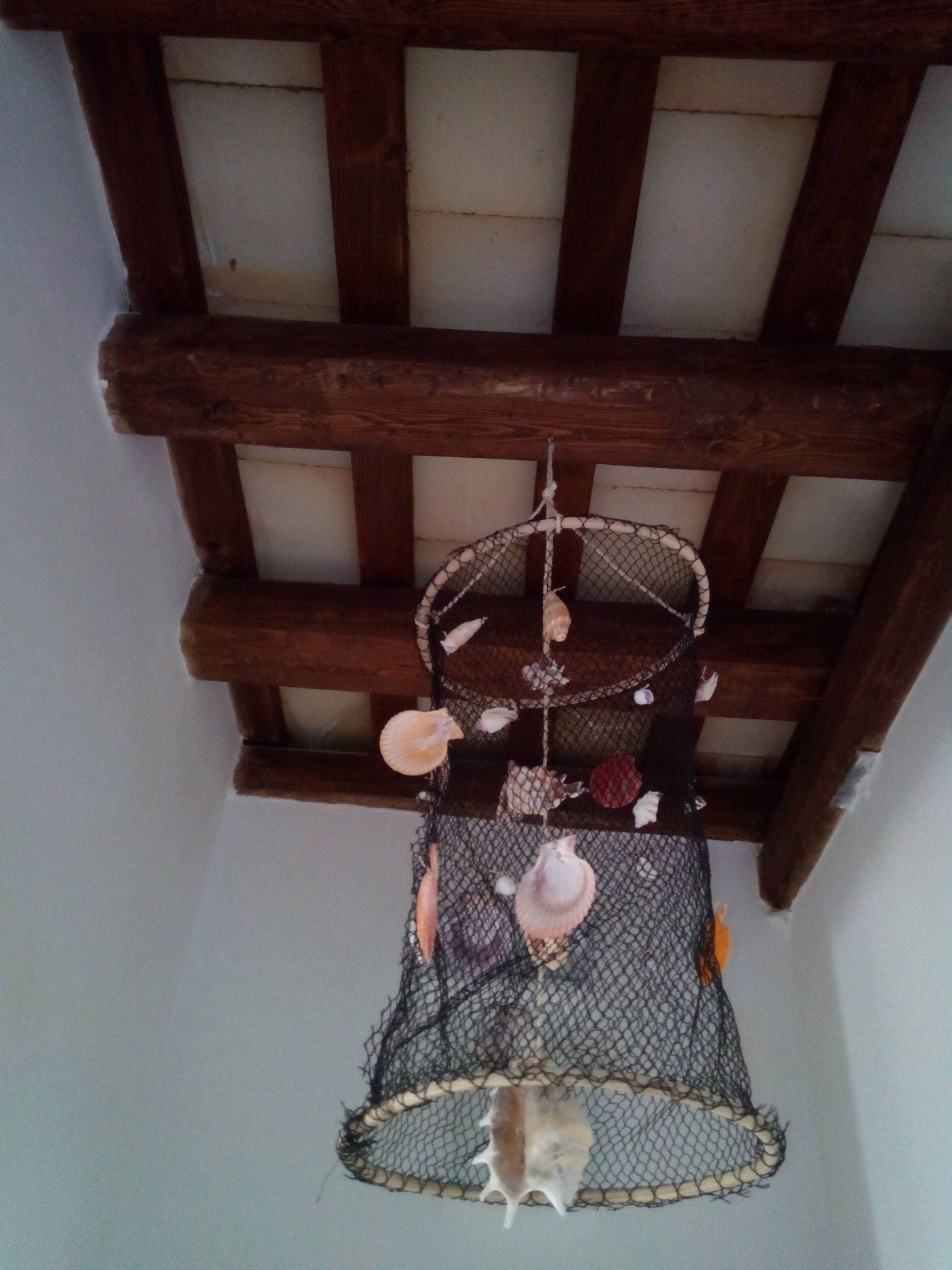A room with a wooden ceiling and a hanging decorative item with shells and a hanging ornament.