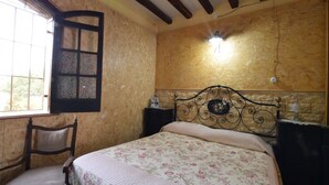 A bedroom with a bed, a chair, a window with a decorative frame, and a wall-mounted light fixture. - Country Cottage / Gite - Siracusa (Siracusa)