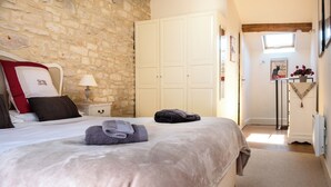 Ein Schlafzimmer mit Steinwand, einem Bett mit beiger Decke, einem Nachttisch mit Lampe und einem Kleiderschrank.