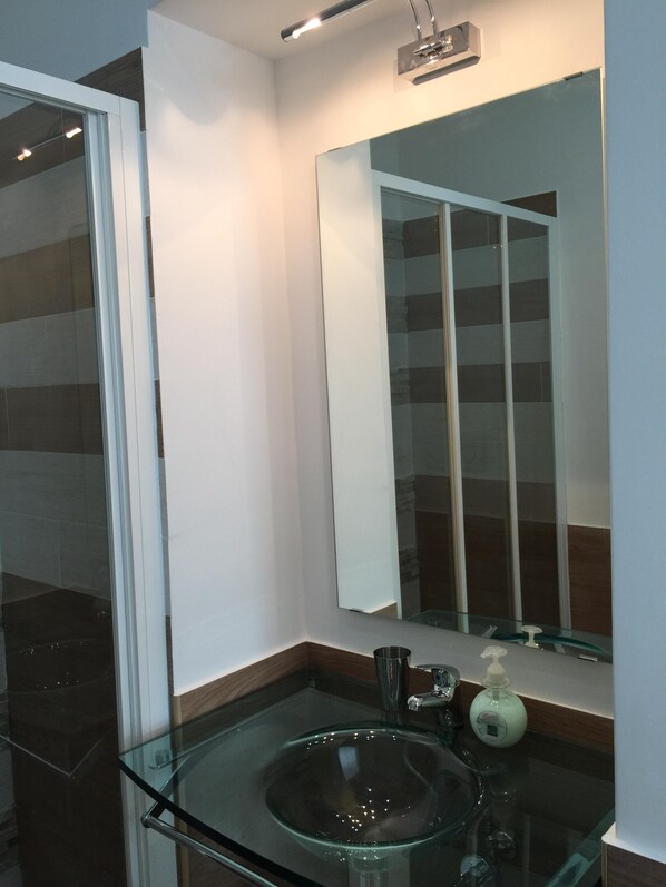 A modern bathroom with a glass sink, a large mirror, and a shower area.