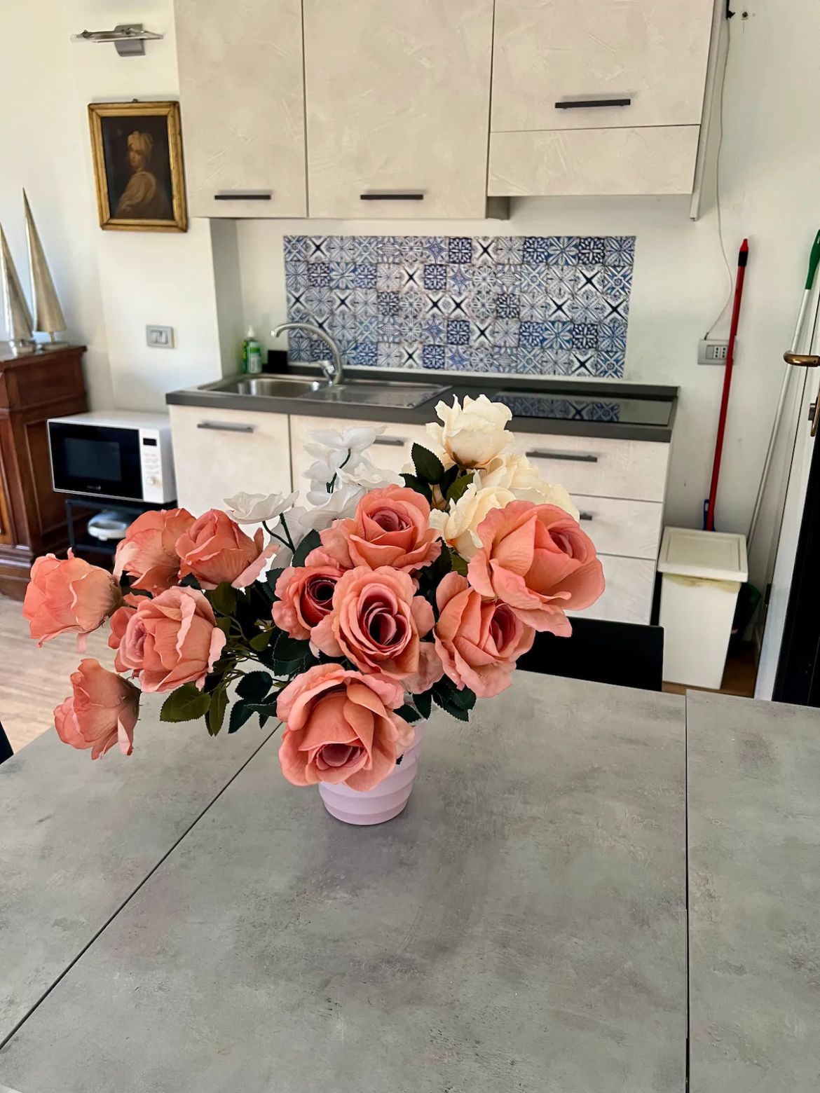 Eine Küche mit hellen Schränken, einer gemusterten Spritzschutzleiste und einer Tischvase mit künstlichen Rosen.